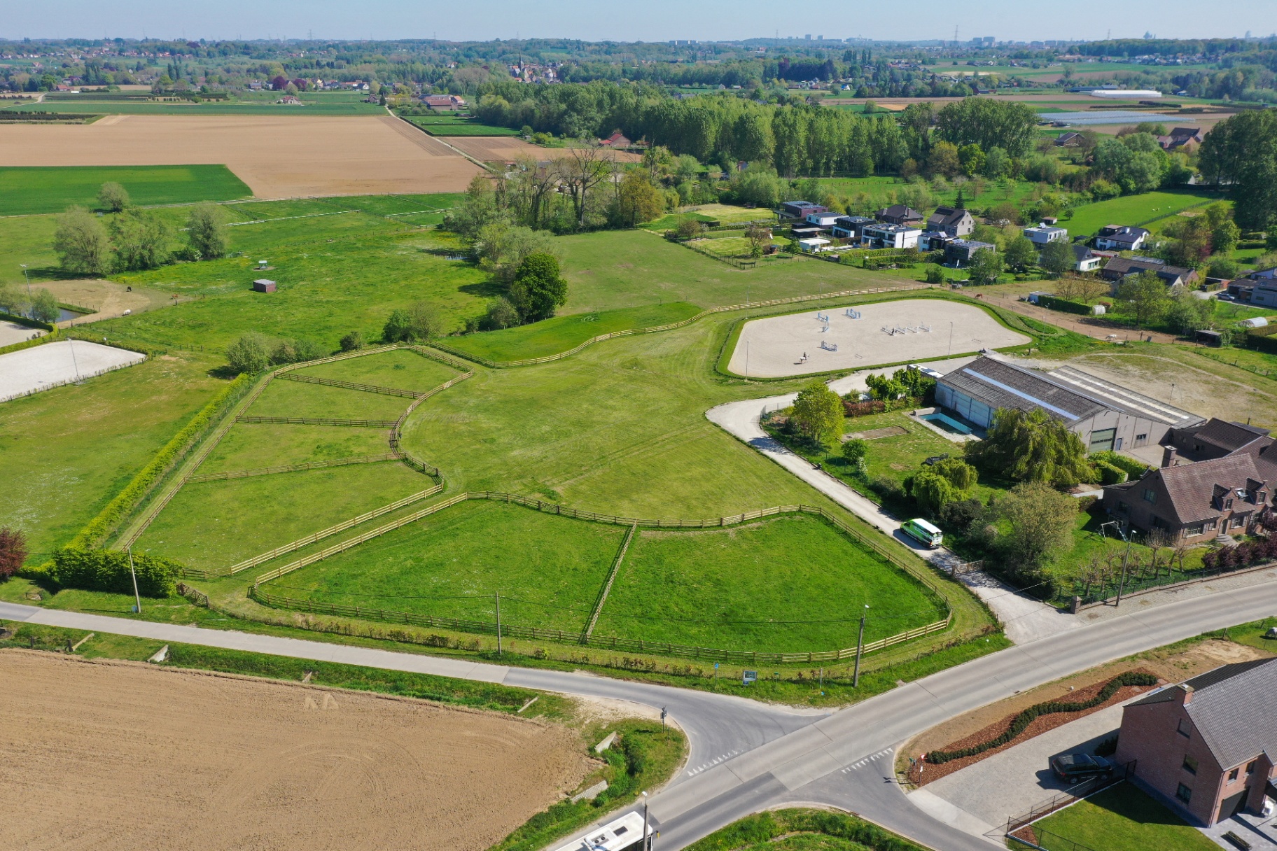Luchtfoto van weides met houten omheiningen naast een paardenaccommodatie