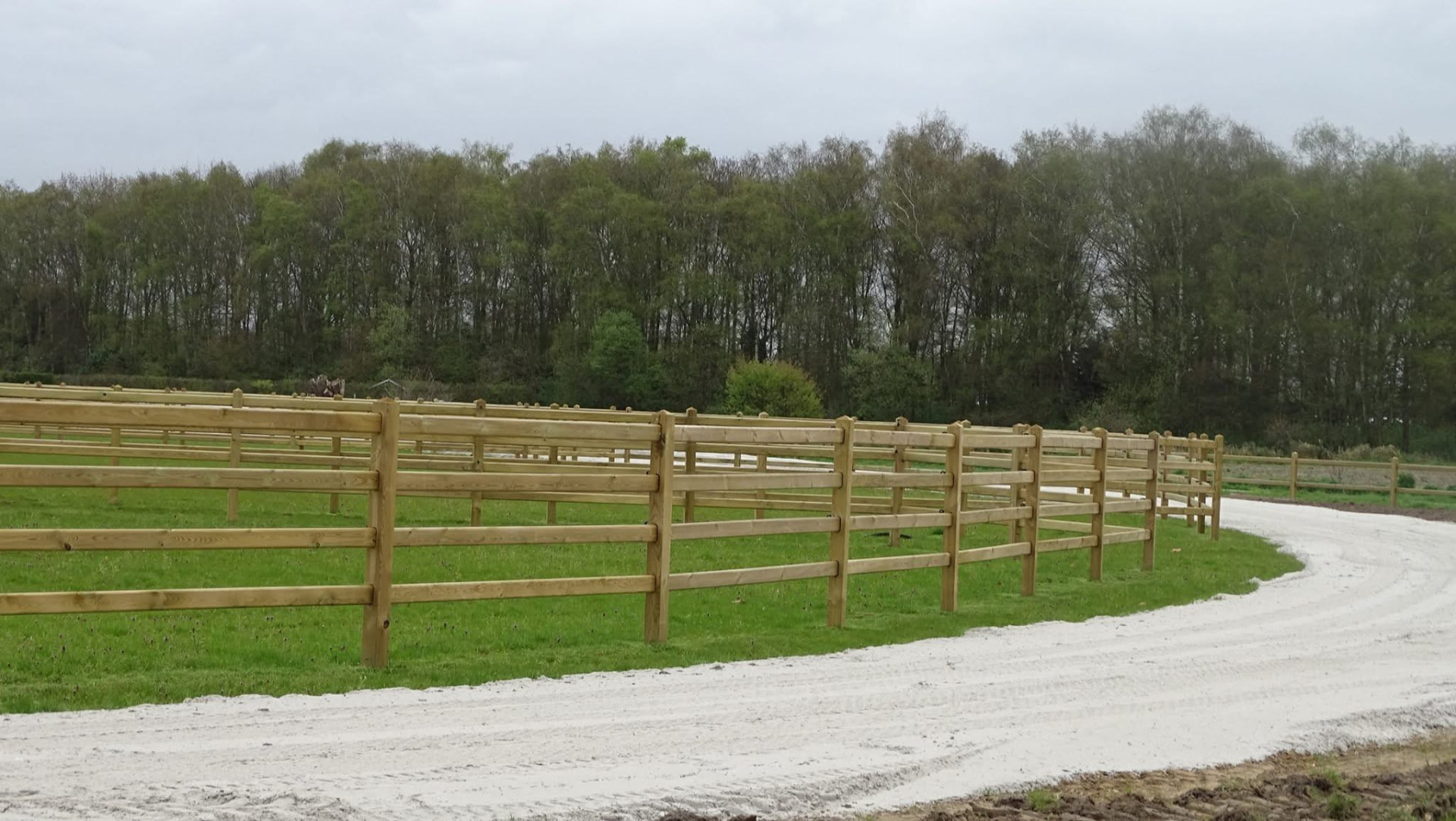 Enjoy-omheining langs een witte zandweg met bos op de achtergrond