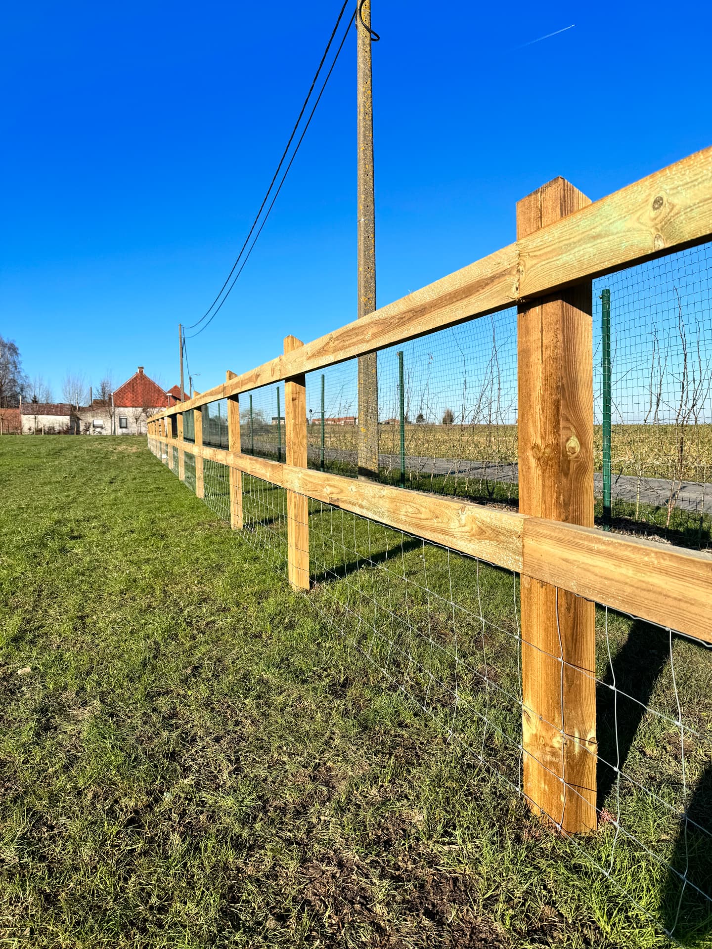 Hennessy-omheining met twee liggers en draadwerk langs een weide, houten palen met schuine kop