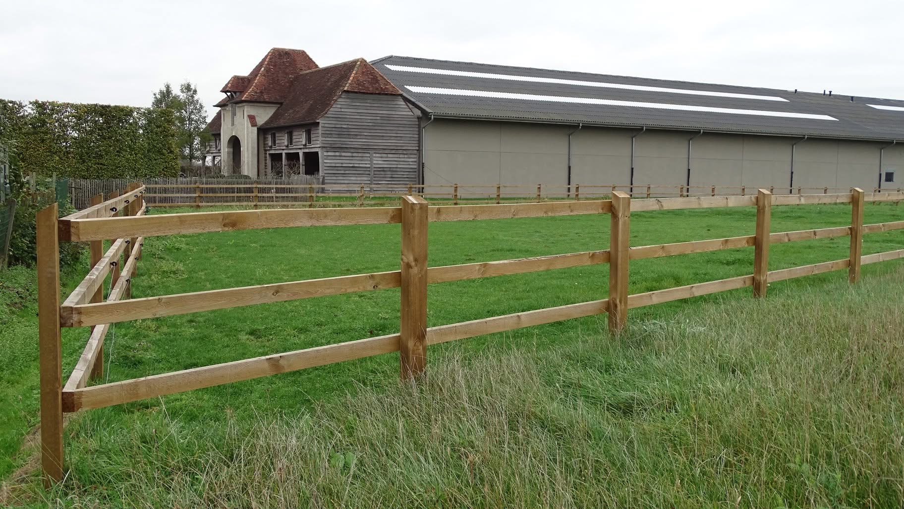 Hennessy-omheining met drie liggers rond een weide, met stalgebouw op de achtergrond