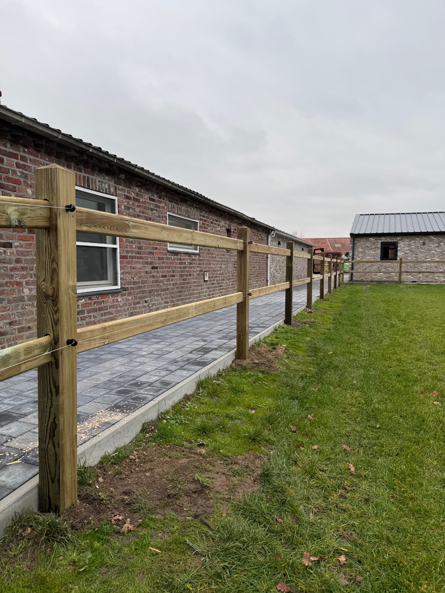 Enjoy-omheining langs een verhard pad met een bakstenen gebouw op de achtergrond